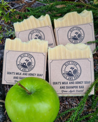 Four bars of soap with labels on a natural background and a green apple in front