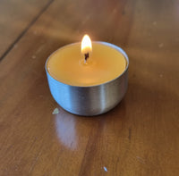 A burning wax tealight candle in a silver reusable case on a wooden table