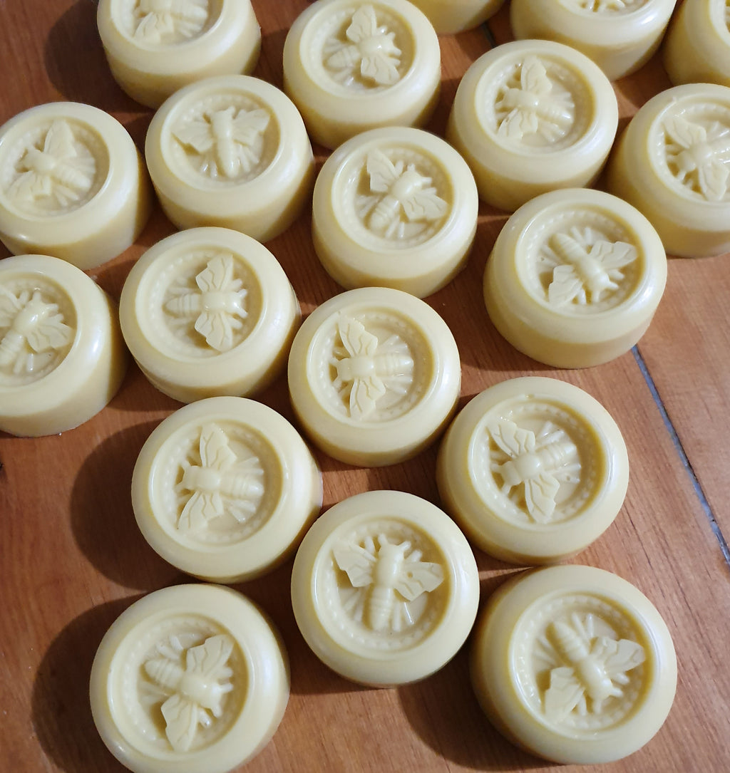 White lotion bars with bee designs on a wooden surface