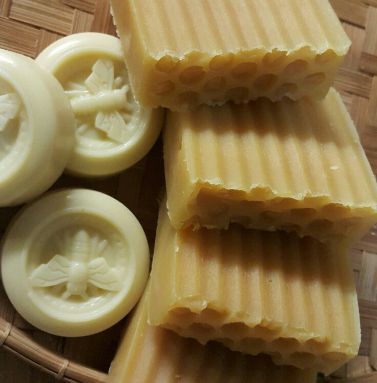 Handmade soap bars with a textured surface and three round lotion bars featuring a bee mold on a woven background.