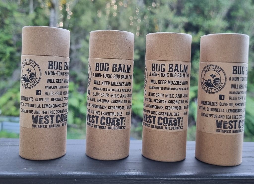 Four cylindrical containers of natural Bug Balm with West Coast branding on a blurred natural background.