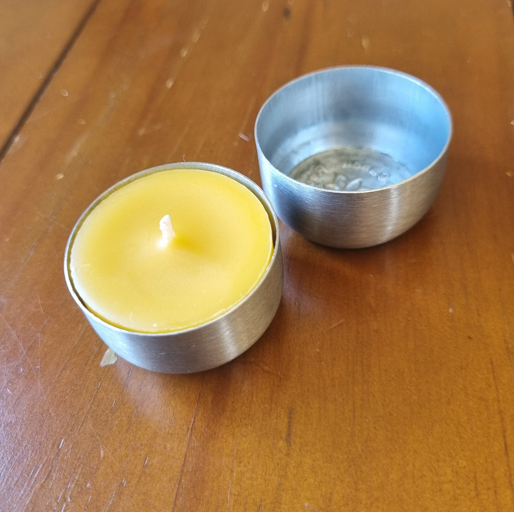 Yellow candle in a metallic container on a wooden surface next to an empty metal container