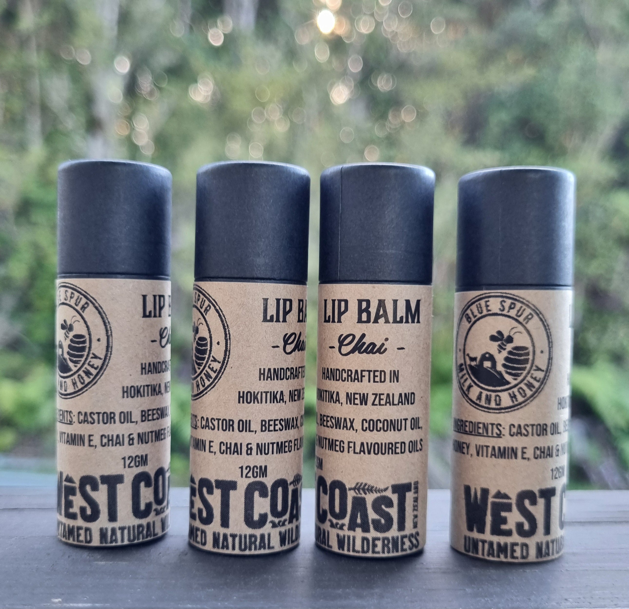 Four lip balm containers with 'West Coast' branding on a blurred natural background