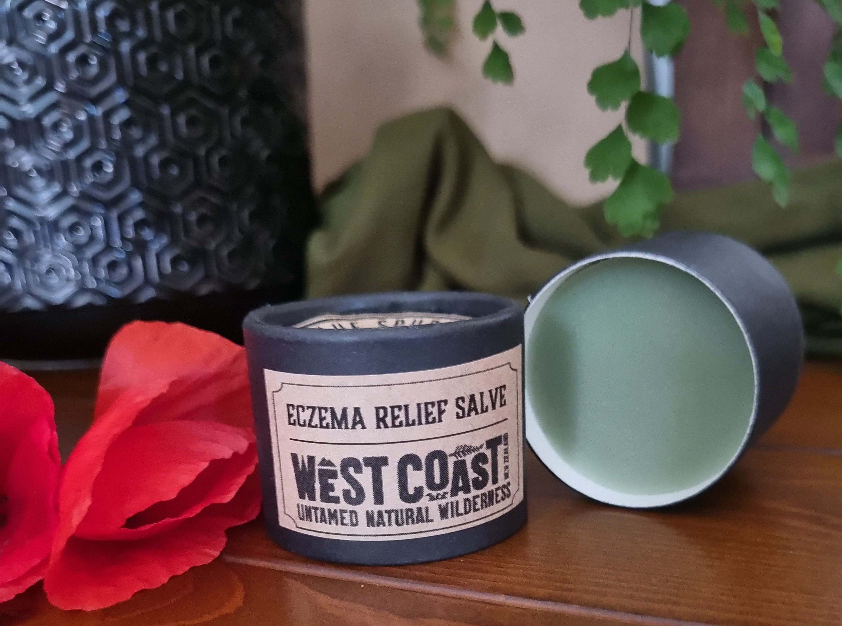 West Coast Eczema Relief Salve container with a red flower and green leaves on a wooden surface