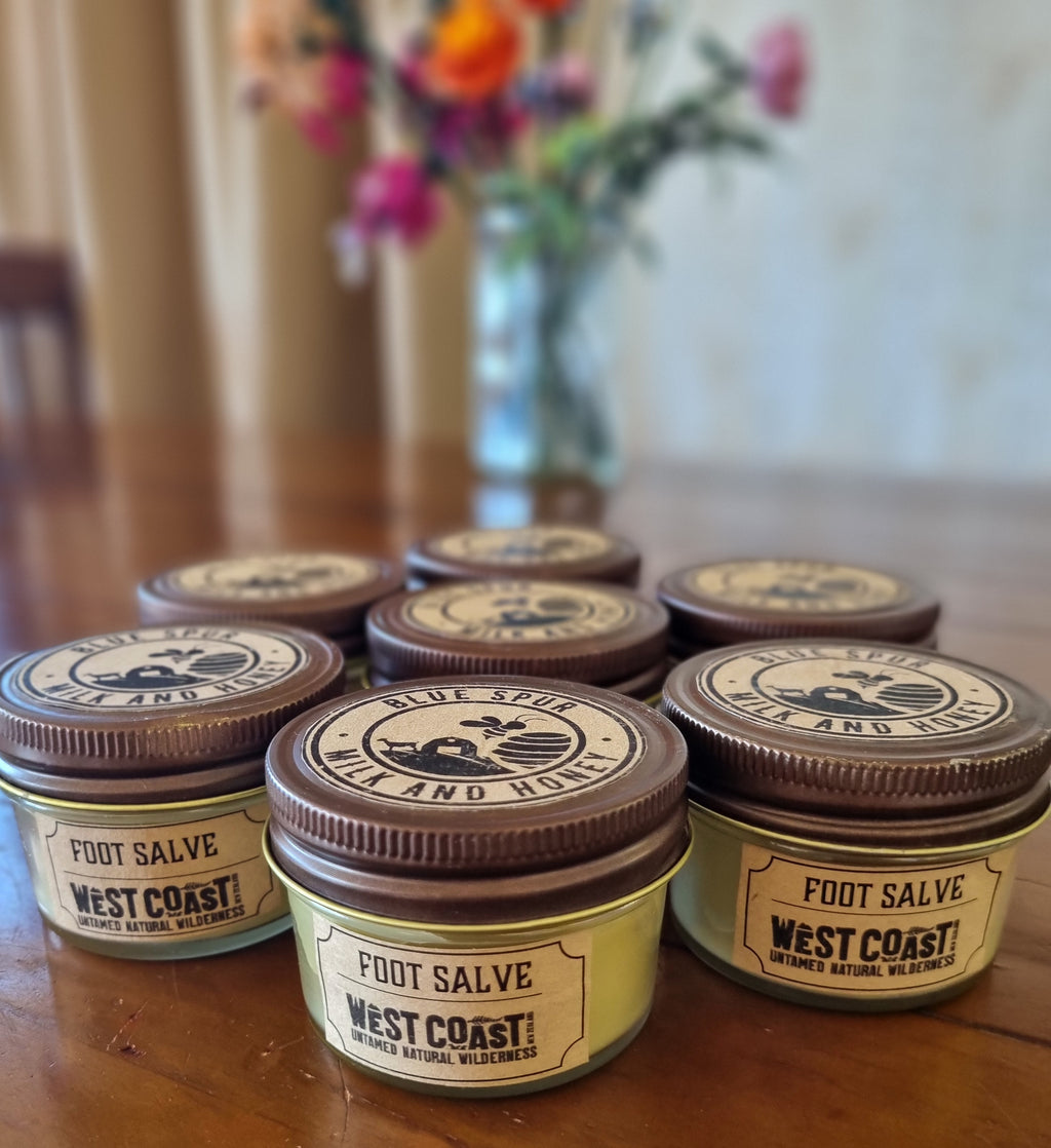 Jars of West Coast Foot Salve on a wooden surface with a blurred background