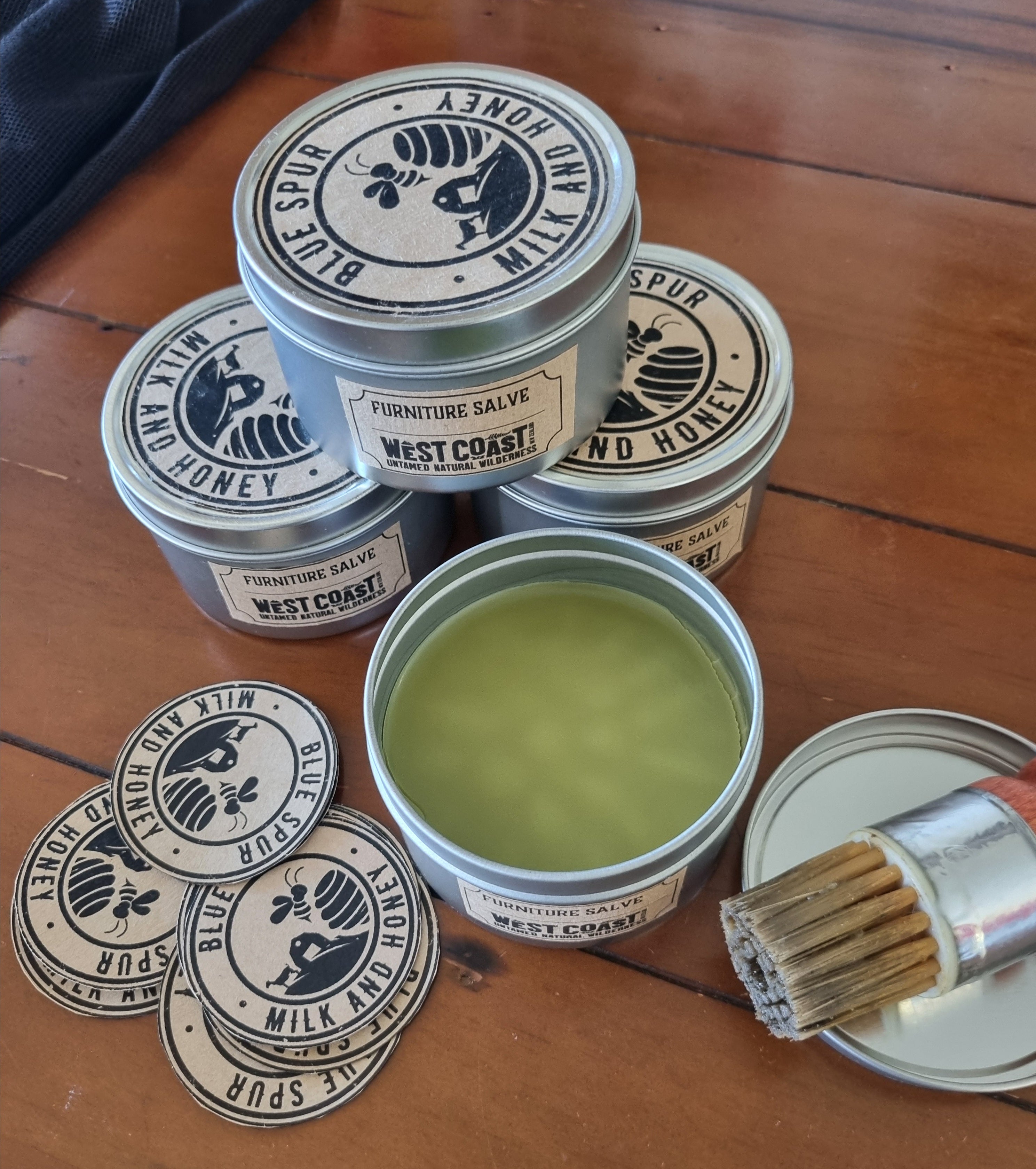 Jars of furniture salve with a brush on a wooden surface