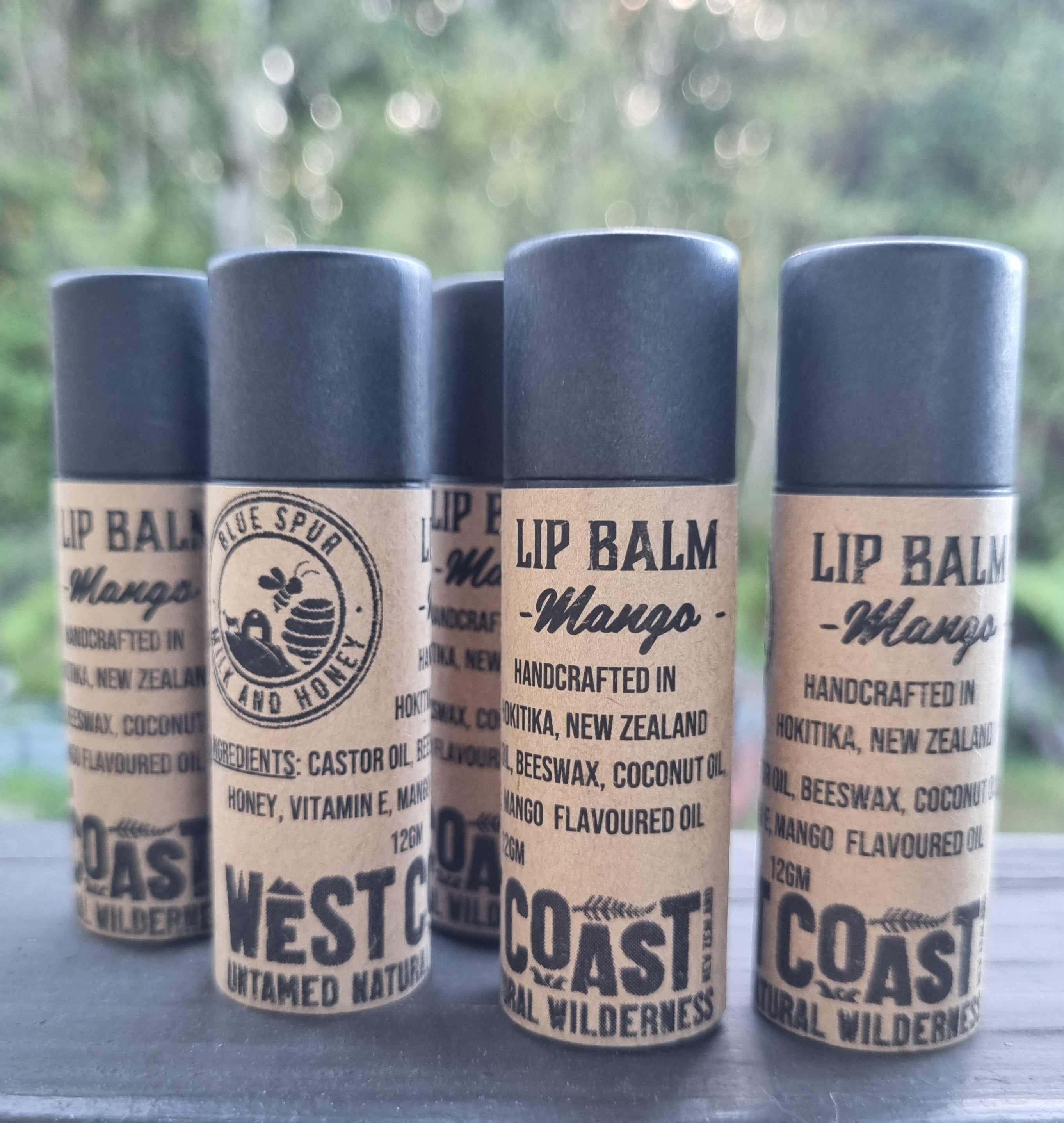 Four lip balm containers with 'Blue Spur and Honey' branding on a blurred natural background.