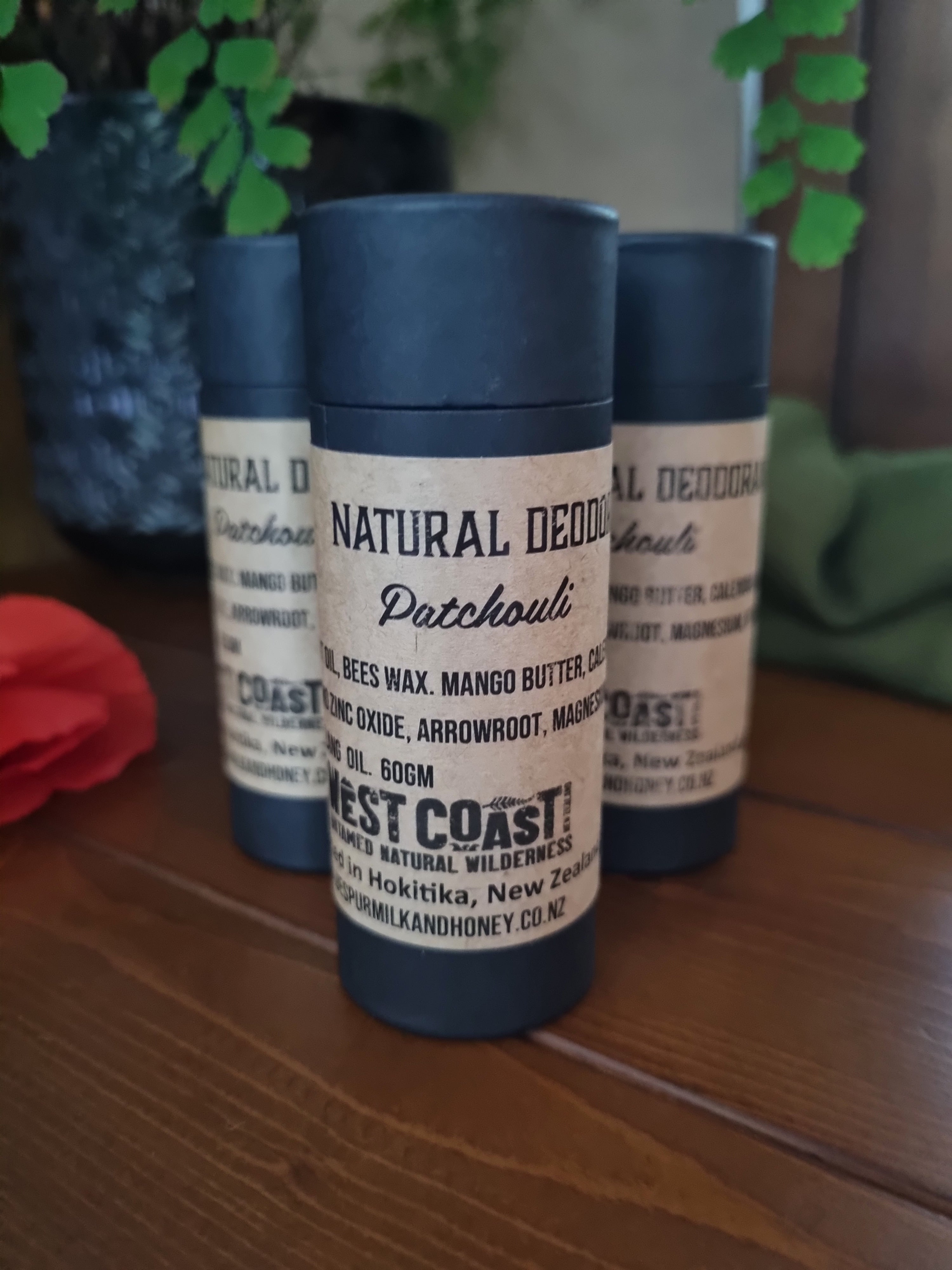 Three patchouli natural deodorants in black paperboard containers with natural labels with a red oppy
