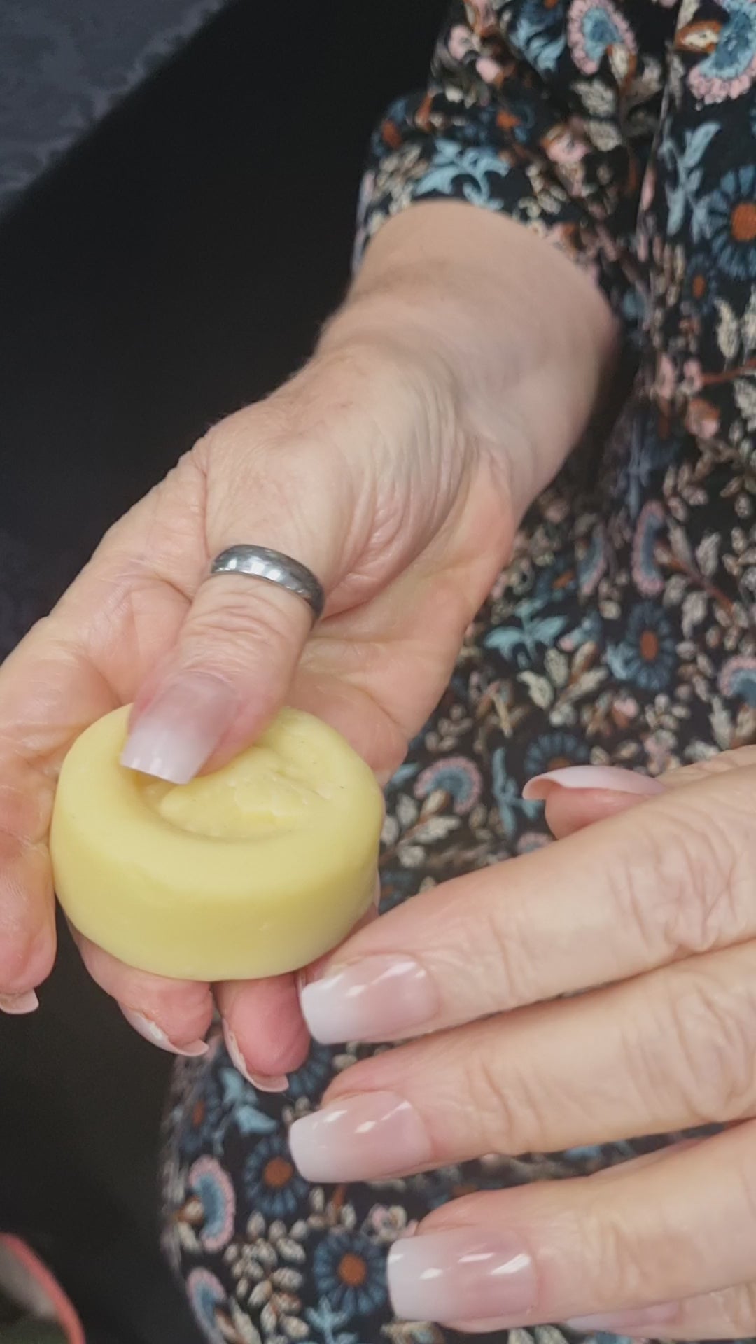 video of two hands rubbing a lotion bar with dark floral fabric as background