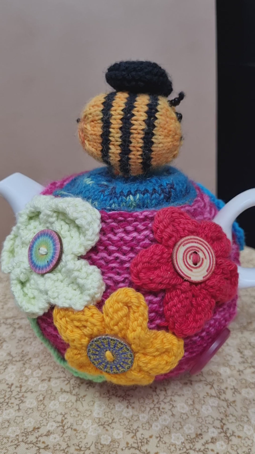 Knitted wool tea cozy with a bee on the top and flowers with buttons