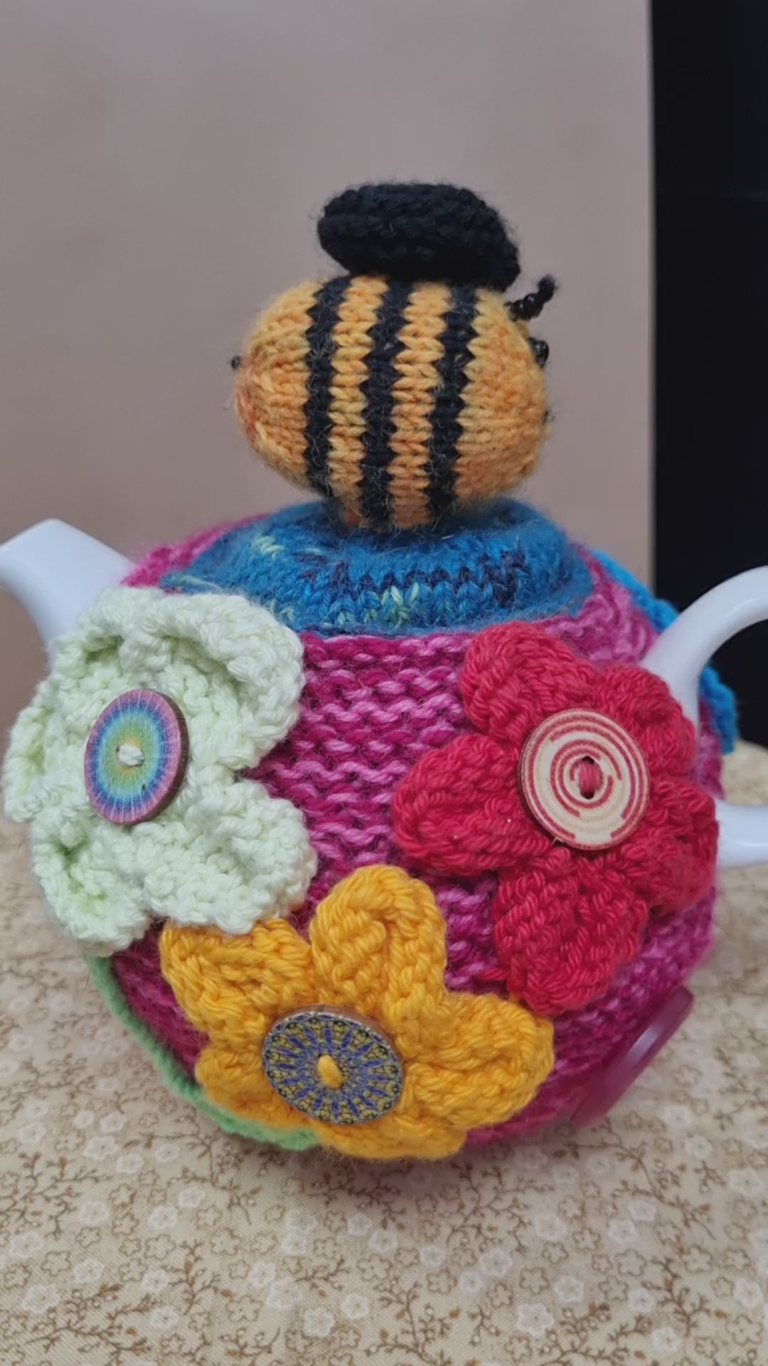 Knitted wool tea cozy with a bee on the top and flowers with buttons