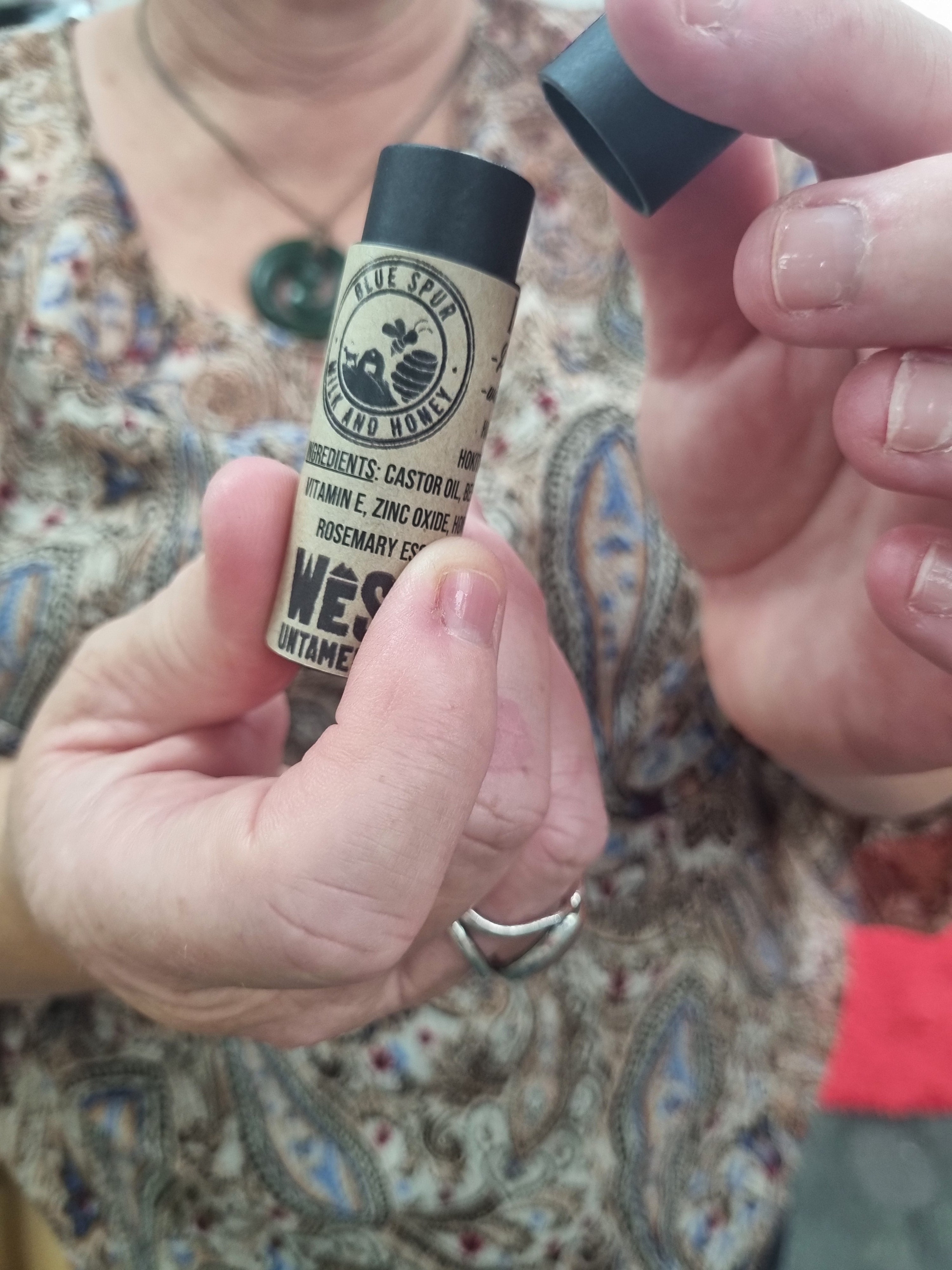 Hand holding a small cylindrical object with a label against a patterned fabric background