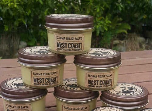 A pile of glass jars with Eczema relief salve on a wooden table with bush behind