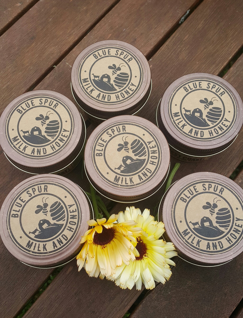 The tops of six glass jars with Blue Spur Milk and Honey  and yellow flowers