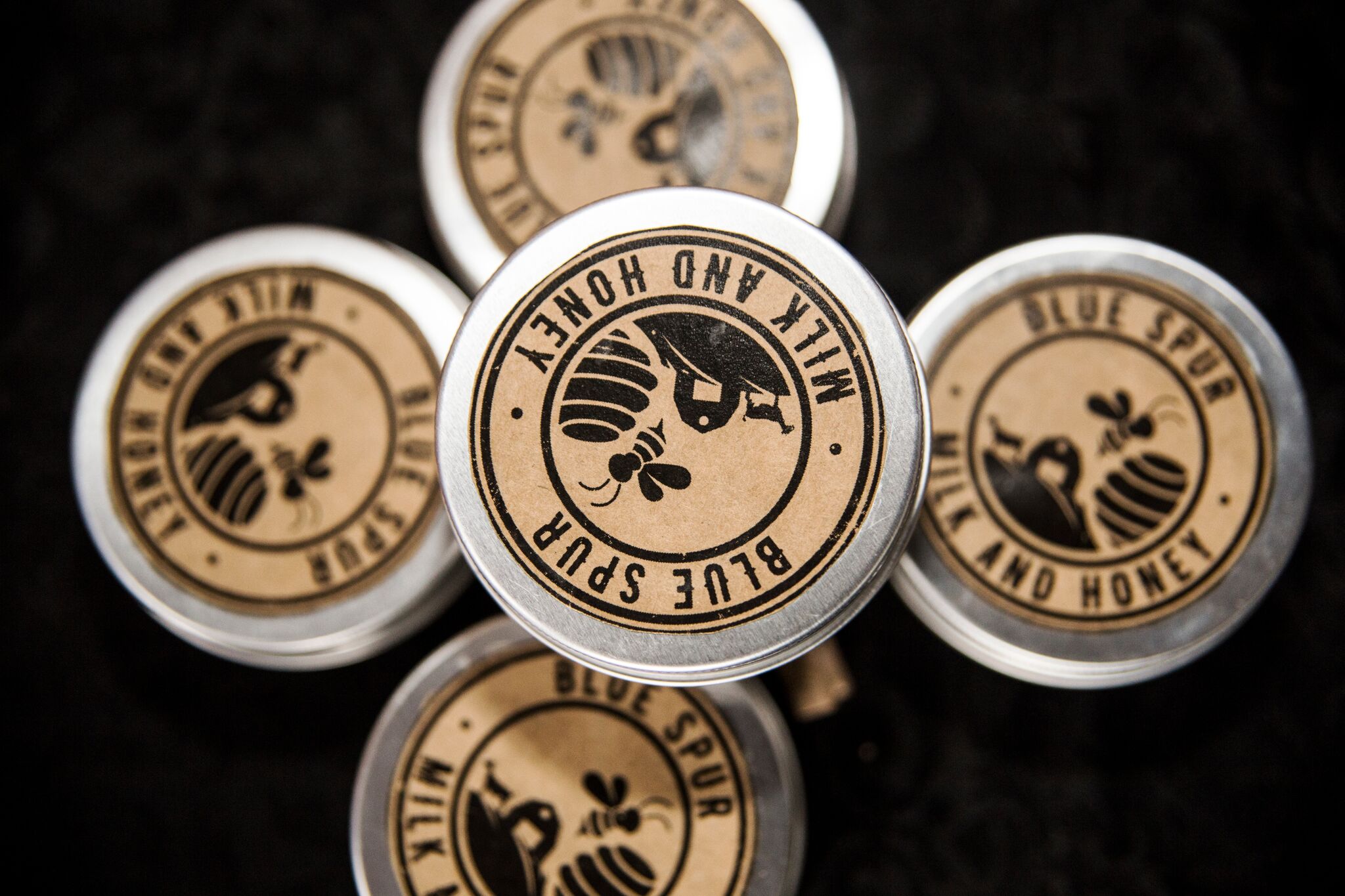 A group of four cylindrical metal tins with a design that includes a honeycomb pattern and the words 'Blue Spur Milk and Honey'.